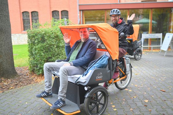 Auf dem Bild sieht man eine Person, die in einer Rikscha gefahren wird.