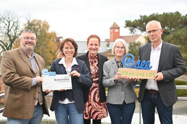Auf dem Bild sieht man zwei Männer und drei Frauen wie sie in die Kamera lachen.