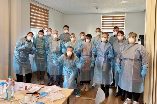 Auf dem Bild sieht man 12 Männer und Frauen mit Maske und Schutzkleidung