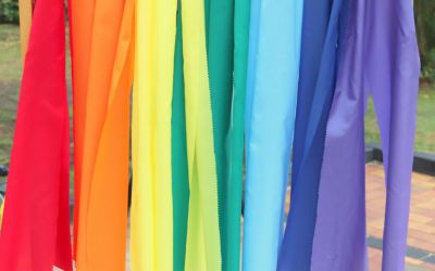 Auf dem Bild sieht man bunte Tücher, die zusammen einen Regenbogen ergeben.