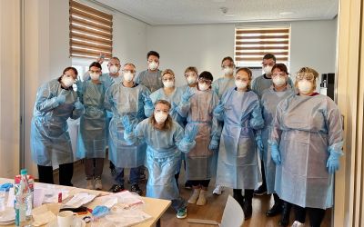 Auf dem Bild sieht man 12 Männer und Frauen mit Maske und Schutzkleidung