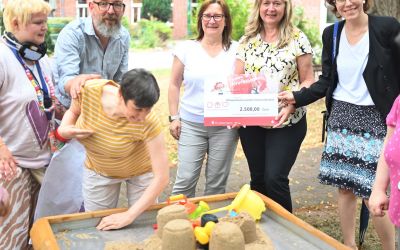 Auf dem Bild sieht man viele Menschen, die einen großen Scheck hochhalten.