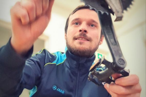 Auf dem Bild sieht man einen jungen Mann, der an einem Fahrrad schraubt.