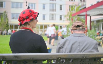 Auf dem Bild sieht man zwei Personen auf der Bank sitzen. Links sitzt eine Frau in Marichen-Kostüm.